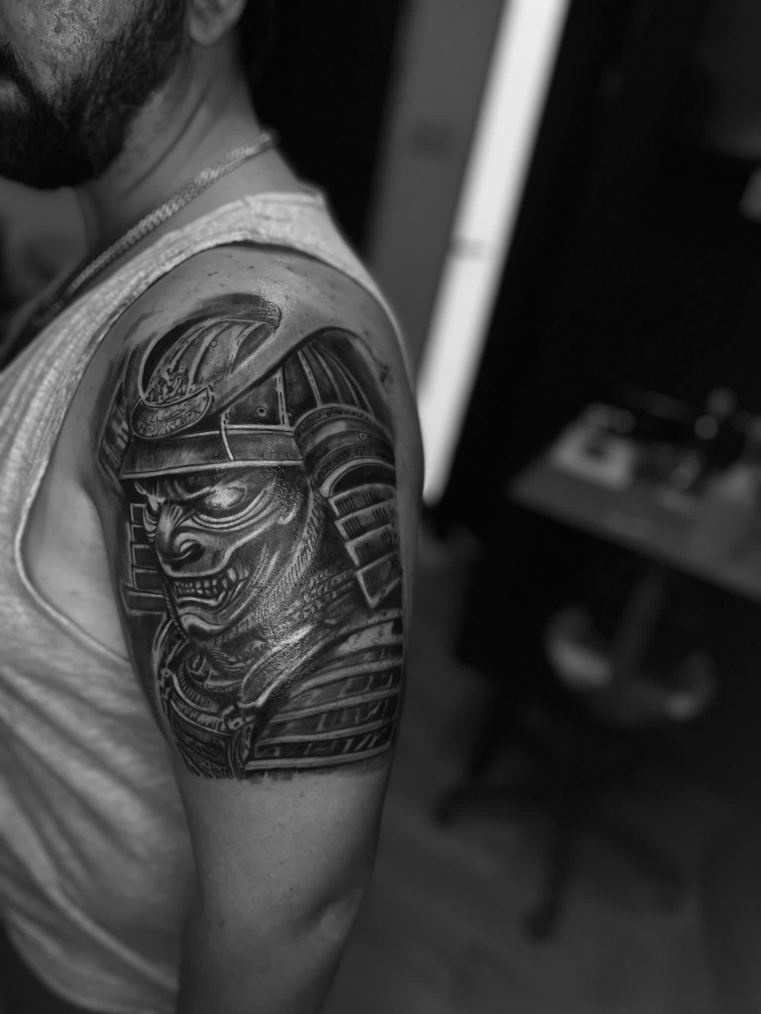 Samurai in a menpō war mask, black-and-grey realism, upper arm — by Stefan Buttigieg at Ink Alley, Żabbar